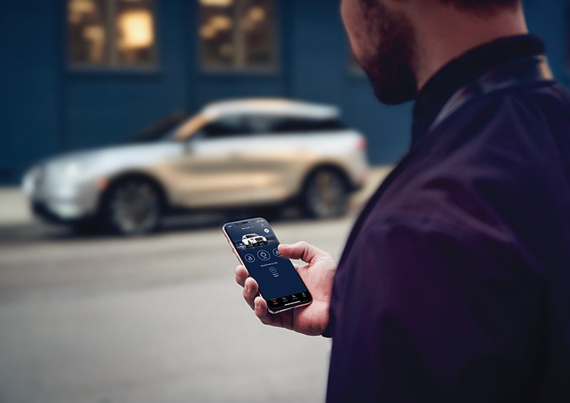 A person is shown interacting with a smartphone to connect to a Lincoln vehicle across the street. | Greenwood Lincoln in Bowling Green KY