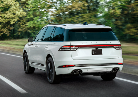 A white 2025 Lincoln Aviator® SUV is being driven away down a road lined with colorful trees. | Greenwood Lincoln in Bowling Green KY