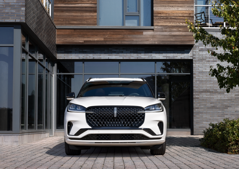 A white 2025 Lincoln Aviator® SUV is shown parked outside a modern building with gray brick and wood accents. | Greenwood Lincoln in Bowling Green KY