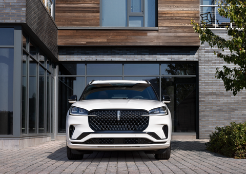 A white 2025 Lincoln Aviator® SUV is shown parked outside a modern building with gray brick and wood accents. | Greenwood Lincoln in Bowling Green KY