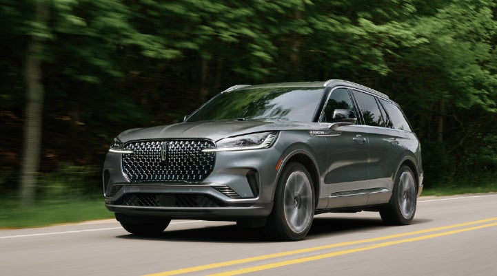 A 2027 Lincoln Aviator® SUV is being driven down a road lined with trees. | Greenwood Lincoln in Bowling Green KY